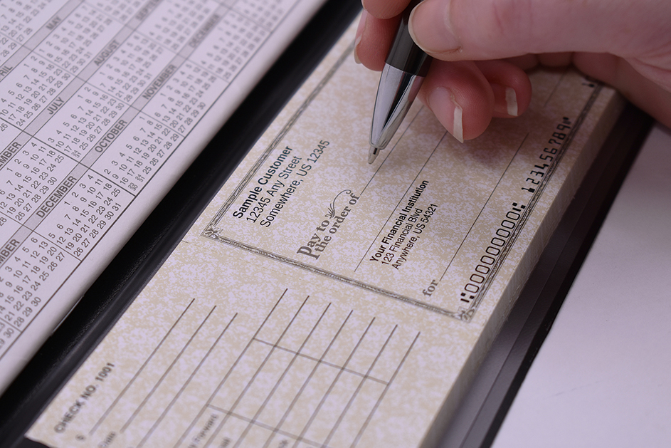  A person using a pen to write in a checkbook with deposit slip.